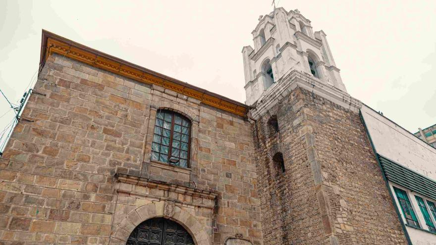 View from below of the church's facade, constructed of stone and white concrete. Its tall white tower is a prominent feature