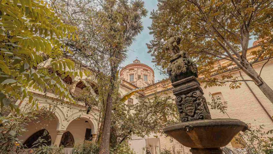  Interior del museo con un patio jardín rodeado de altos árboles y una fuente de agua en piedra tallada.