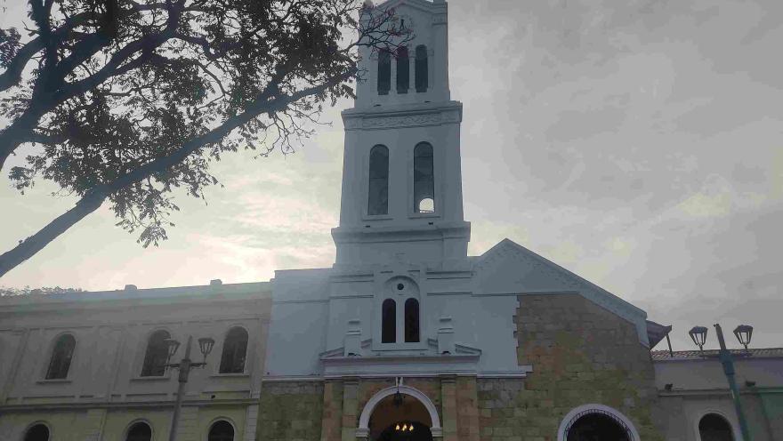 Front view of the church facade, highlighting its structure of stone and white concrete, the tall bell tower, and its arched entrance.