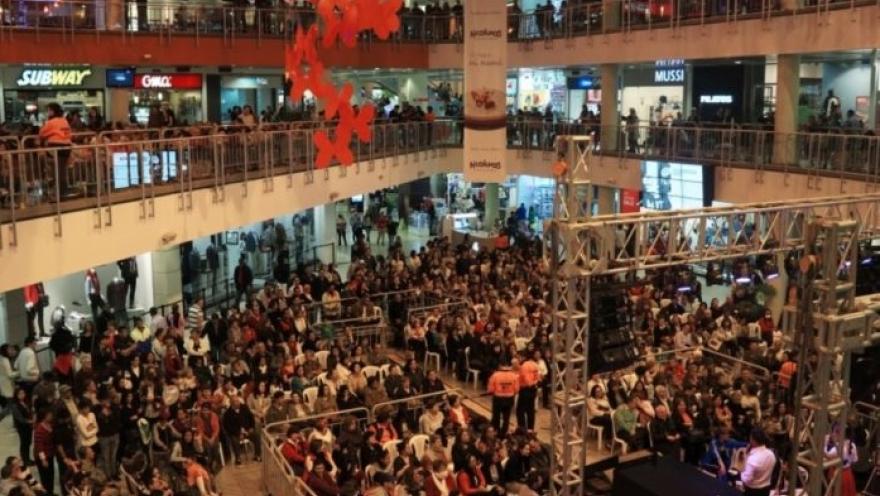Interior de centro de comercio en el que se observan tres pisos con locales comerciales repletos de personas.
