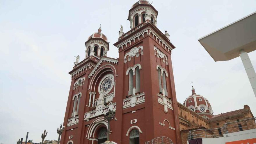 A close-up of the church facade seen from below. The arched main entrance is visible, and in the background, a dome is visible behind the roof.