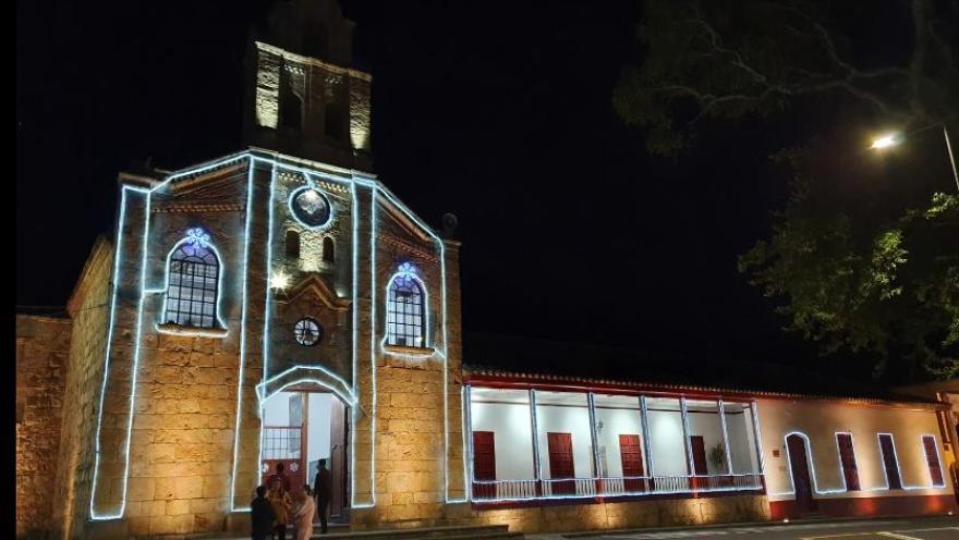 Panorámica de la fachada de la parroquia de noche y adornada con luces de neón.