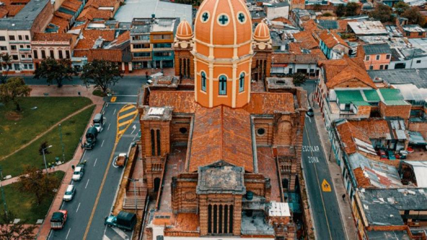 Panorámica de una iglesia vista desde arriba, como con un dron. Sobresalen los techos de ladrillo y una torre alta en forma ovalada y de color naranja.