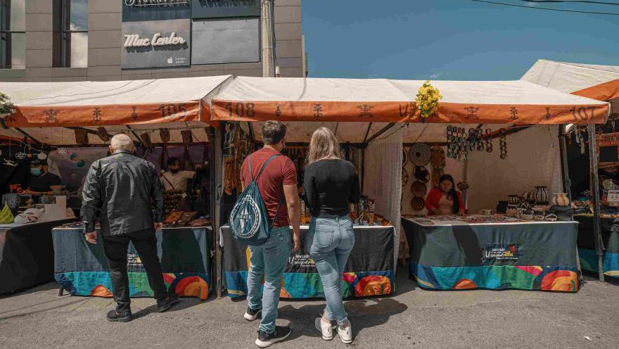 Un hombre y una mujer joven parados al frente de un toldo de comercio, parece que observando artesanías.