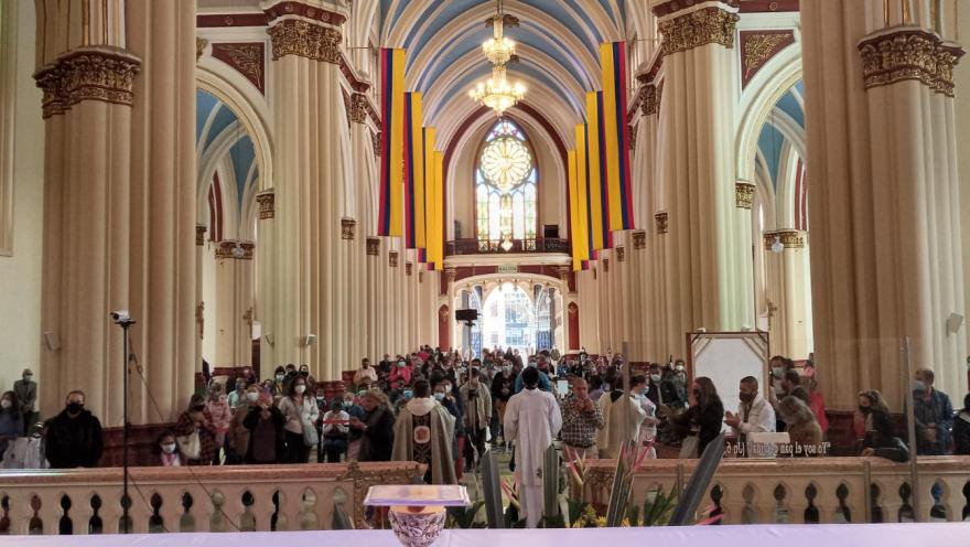 Panorámica del interior de la iglesia en la que destaca que está repleta de personas y hay unas banderas de Colombia que cuelgan en la parte alta.