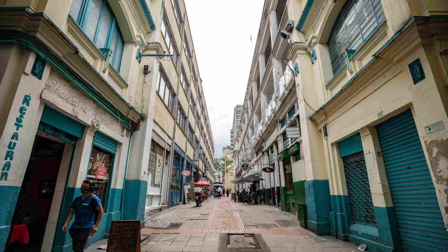 Una calle entre edificaciones antiguas por la que camina un hombre joven con tapabocas.