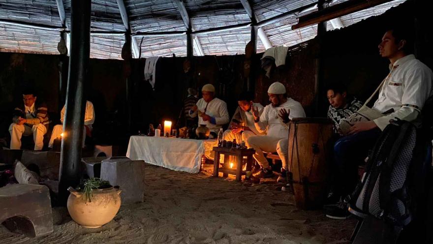 Un grupo de personas sentadas alrededor de un fuego en una cabaña, estilo maloka, compartiendo historias y disfrutando del calor.