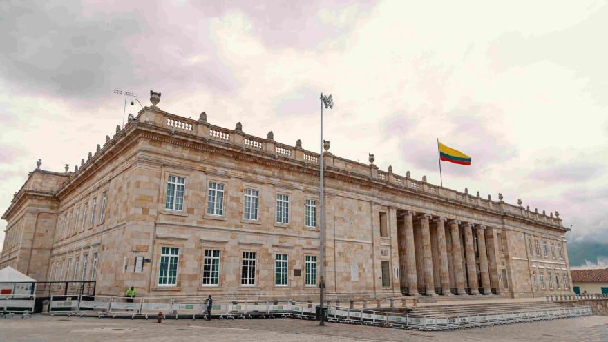 Vista lateral de la fachada del Capitolio Nacional en piedra. Se observan algunas ventanas y la bandera de Colombia izada en lo alto.