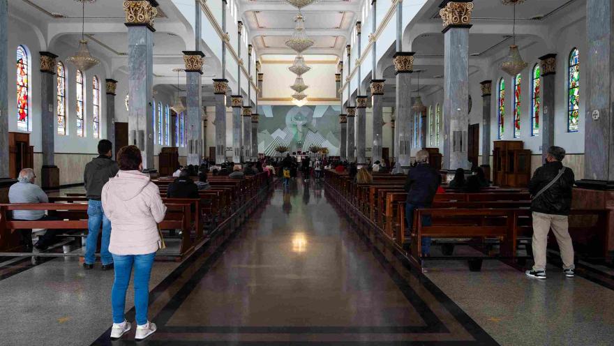Plano general del interior de la iglesia. Al fondo se observa el altar con un gran Cristo y alrededor varias sillas con personas.