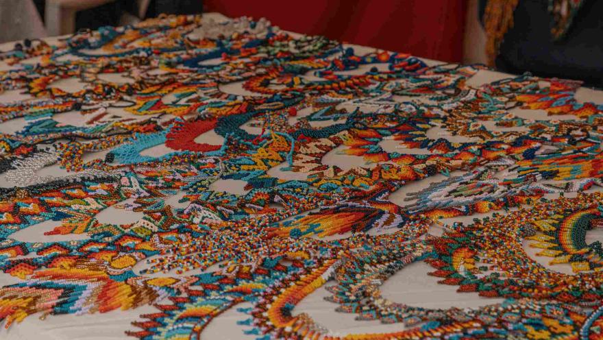  Primer plano de una mesa con varias artesanías como collares y aretes con los colores de la bandera colombiana, amarillo, azul y rojo.