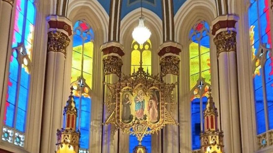 Primer plano de un vitral visto desde abajo en el que destaca la imagen de la Virgen María y de fondo los vidrios con colores amarillo, azul y rojo.