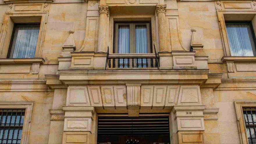 Primer plano de la fachada del edificio de frente en la que se observan tres ventanas en un segundo piso, una de ellas con un balcón.