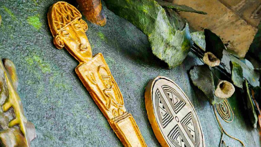 Escultura de arte indígena con figura humana dorada y diseño ovalado.