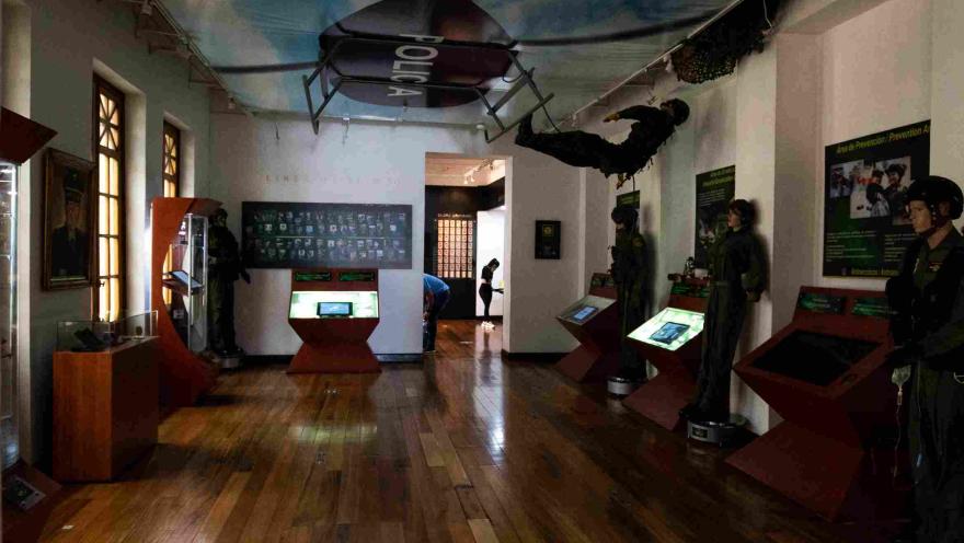 Interior de museo con varias figuras tipo maniquíes de policías. Se destaca en el techo el dibujo de un helicóptero con una leyenda grande que dice “Policía”. Hay un maniquí que se descuelga de la imagen de la aeronave.