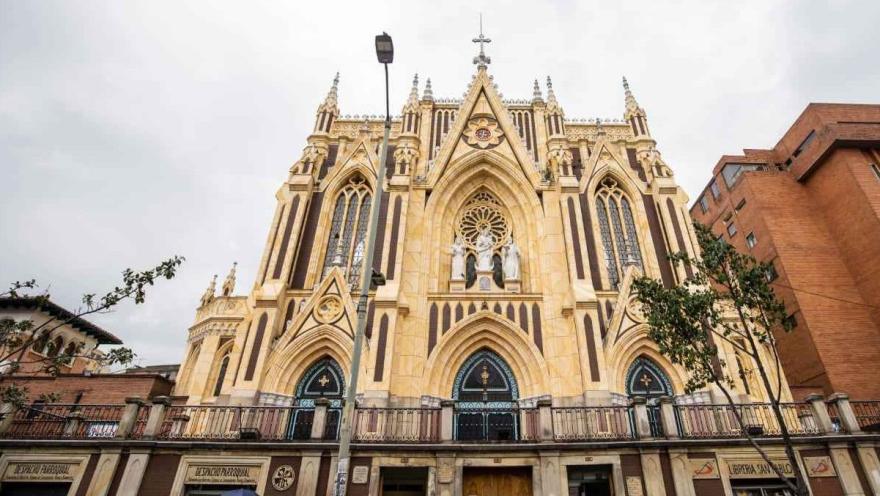 Primer plano de frente de la fachada gótica de la iglesia con algunas edificaciones alrededor. 