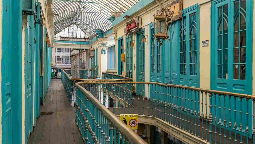  Vista interior de un segundo piso de edificación antigua en la que hay puertas de color azul turquesa y unos pasamanos dorados.