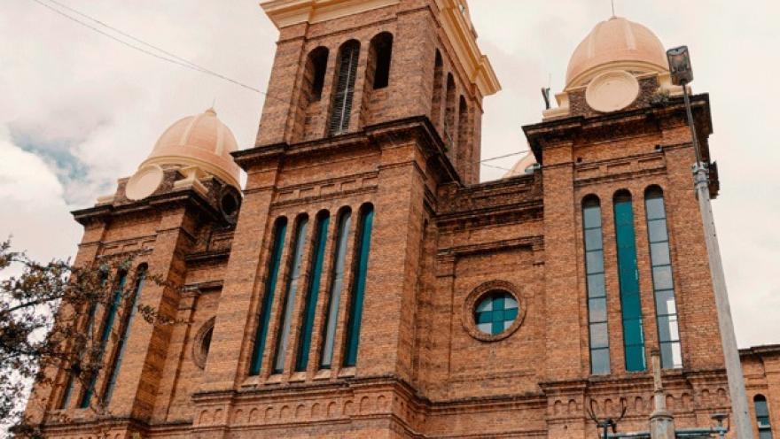 Fachada de iglesia en ladrillo vista de lado. Se observa una torre con un reloj en el centro y tres cúpulas