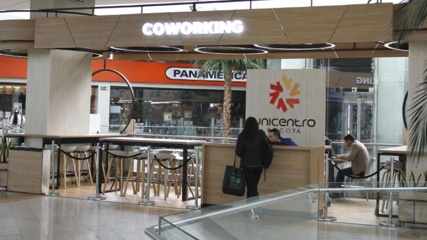Espacio interior en el que se destaca un aviso en neón con letras blancas con una leyenda que dice: “COWORKING”. Hay un hombre joven atendiendo un stand de información en el que se lee la leyenda “Unicentro”.