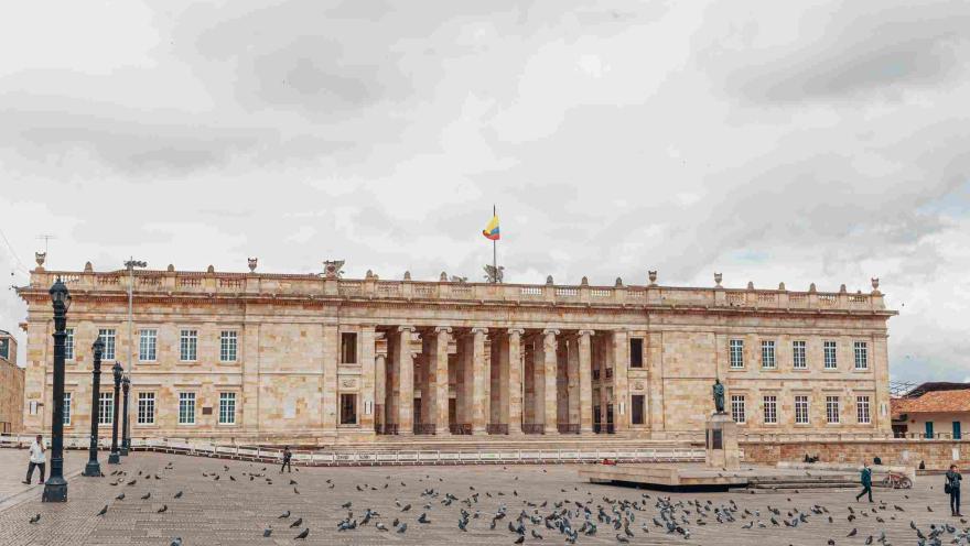 Fachada del Capitolio Nacional en piedra. Se observa al frente la Plaza de Bolívar con algunas palomas alrededor.