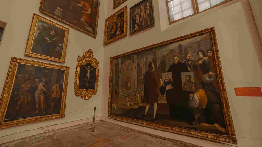 Un cuarto interior con dos paredes abarrotadas con cuadros, parece que religiosos y de época colonial.