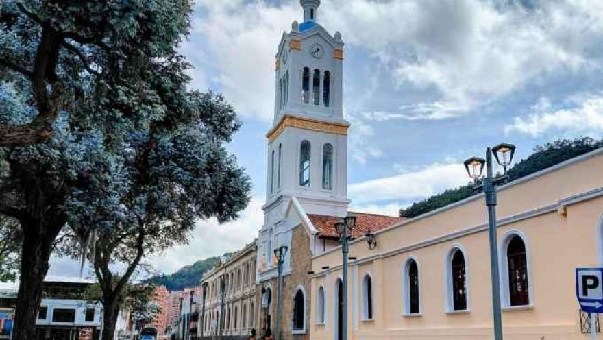 Side view of the church facade, featuring the large clock tower and the tall trees in the foreground in what appears to be a park.