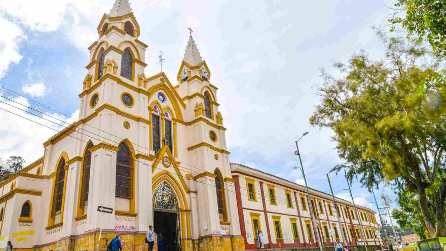 Iglesia con un campanario al lado de la calle, rodeada de árboles y un cielo despejado.