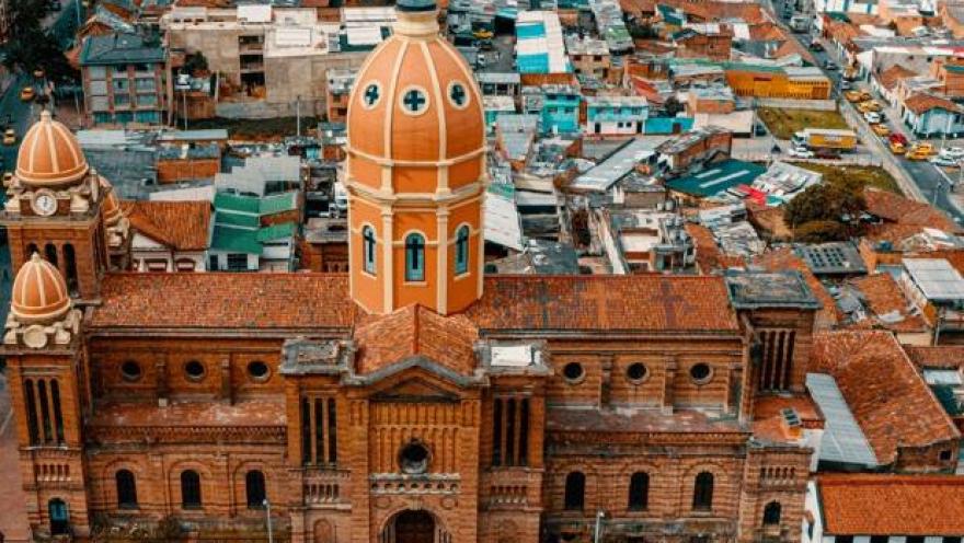 Plano general de una iglesia vista desde arriba, en ladrillo, con una torre de forma ovalada y de color naranja. Hay varias edificaciones alrededor.