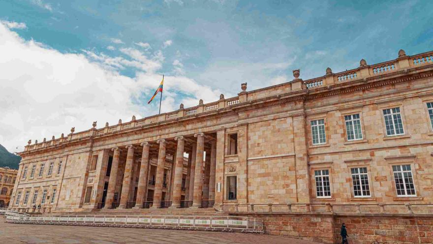 Fachada del Capitolio Nacional en piedra. Se observan algunas ventanas y la bandera de Colombia izada en lo alto.