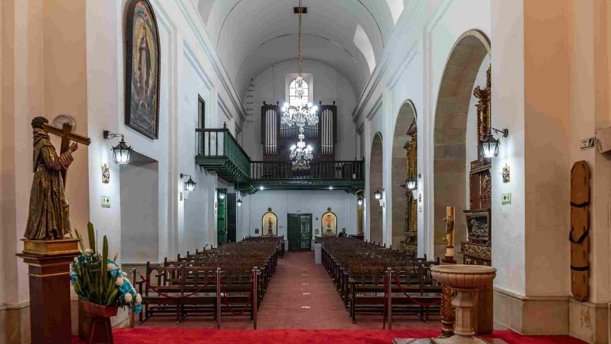  Interior de la capilla principal visto desde el altar hacia las sillas para los asistentes. En el segundo piso se observa un balcón y un gran órgano de madera.