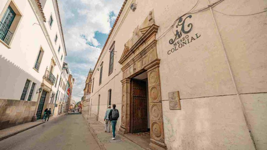 Una calle muy angosta en la que al lado derecho está la puerta en madera robusta de acceso al museo, y que se identifica con un aviso con una leyenda que dice: "Museo Colonial".
