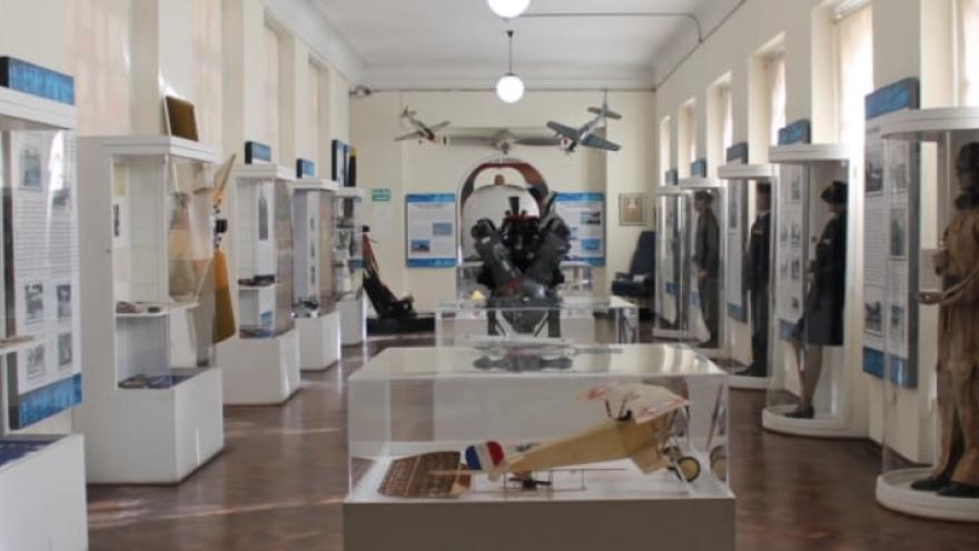 Sala de museo con vitrinas que exhiben objetos históricos militares y de aviación, incluyendo uniformes, maquetas de aviones y paneles informativos dispuestos a lo largo de un pasillo iluminado.
