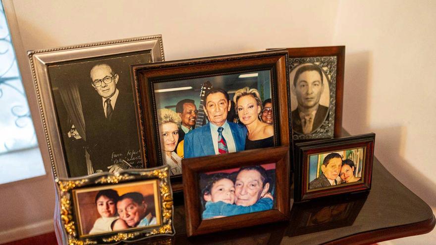 Conjunto de fotografías familiares enmarcadas, dispuestas sobre una mesa de madera. Las imágenes incluyen retratos antiguos en blanco y negro y fotos a color de distintas épocas, mostrando a varias personas en momentos íntimos y afectivos.
