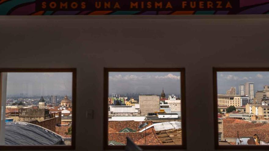  Vista de la ciudad a través de tres ventanas rectangulares desde el interior de un edificio. Se observan techos de tejas rojas, edificios del centro histórico y algunas construcciones modernas al fondo.