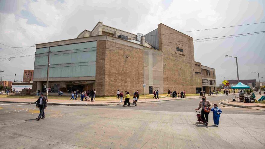 Vista exterior de un edificio cultural moderno de ladrillo y vidrio identificado como “El Ensueño”. Varias personas caminan por la acera y cruzan la calle frente al lugar, en un entorno urbano con cielo nublado.