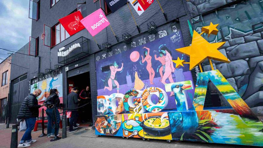 Fachada de edificio gris con vibrante arte callejero y una gran instalación de letras que deletrea "BOGOTÁ" en la acera.