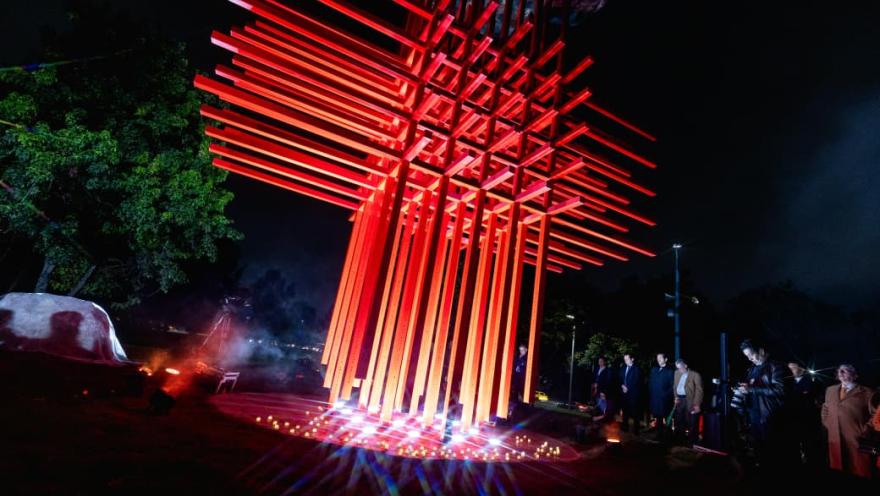  Escultura roja grande con varias personas de pie a su alrededor, admirando la obra artística en un espacio público.