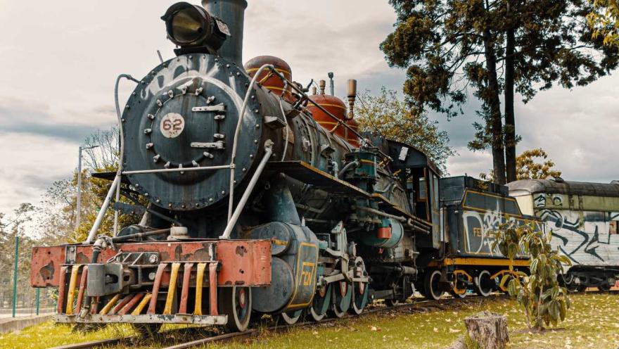 Un tren antiguo en las vías, cubierto de graffiti colorido y desgastado por el tiempo.