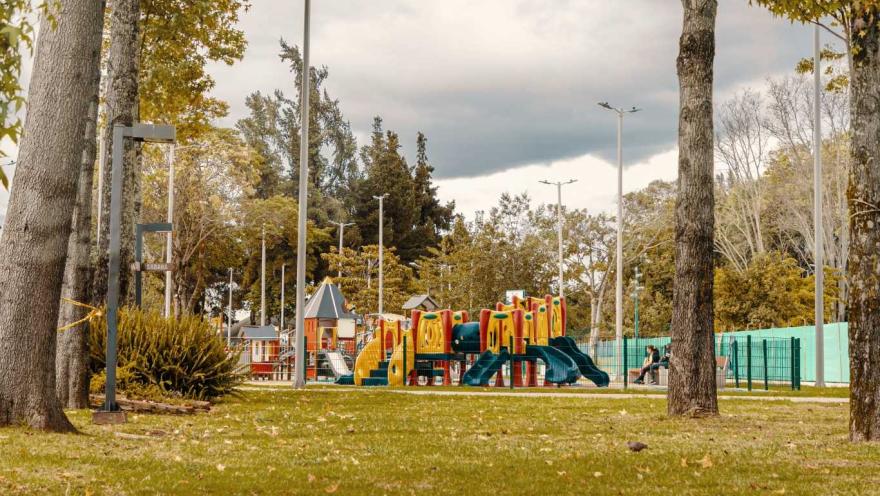 Un parque con un área de juegos y árboles frondosos, ideal para disfrutar al aire libre.