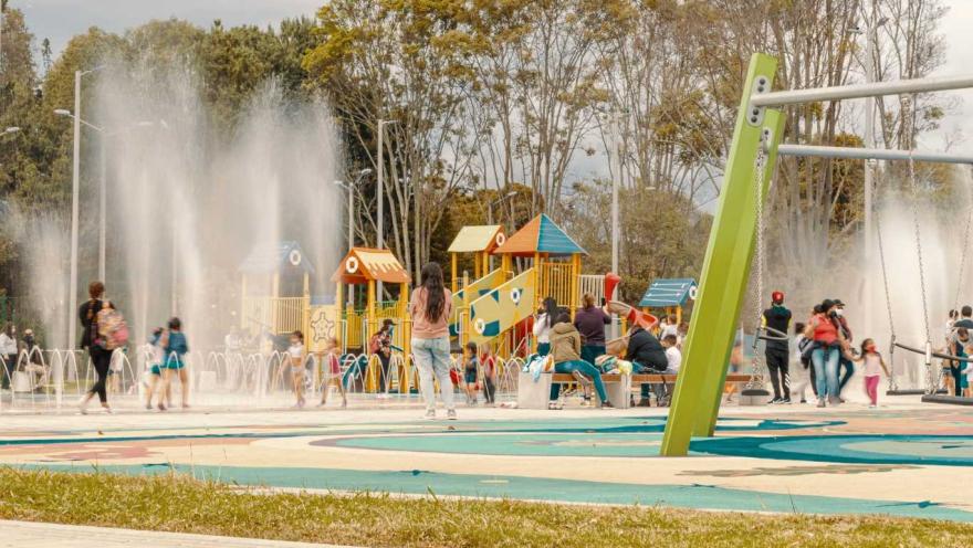Niños jugando en el agua en un parque, riendo y disfrutando de un día soleado.