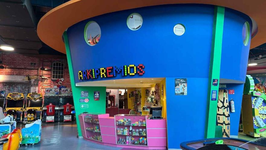 Mostrador de premios en un parque de entretenimiento interior, con fachada colorida y máquinas de videojuegos alrededor.