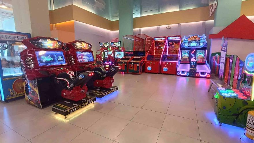 Zona de videojuegos arcade en interior con máquinas de carreras, juegos de canasta y luces de colores.