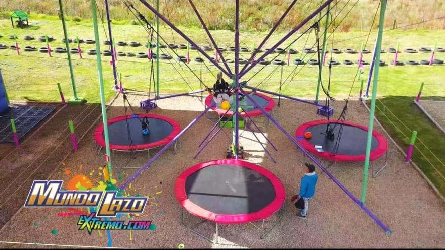  Estructura de trampolines circulares conectados por cuerdas en un parque al aire libre, con personas saltando y supervisando la actividad.