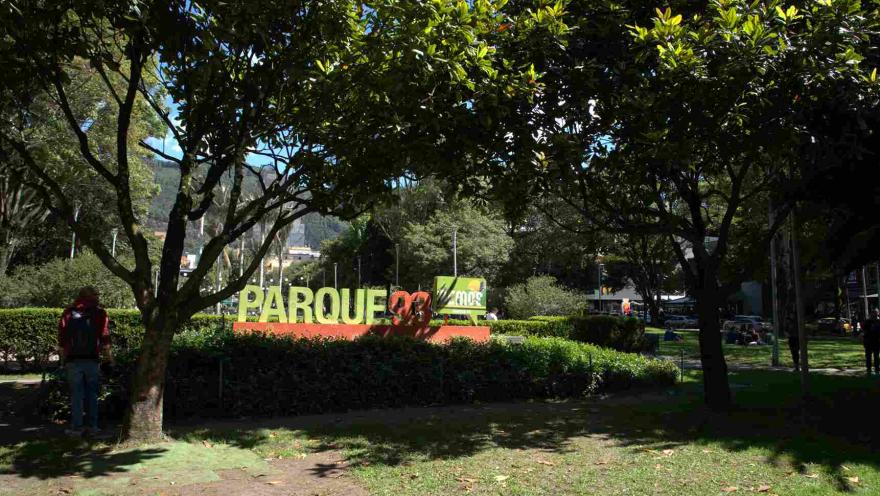 Letrero de “Parque 93” rodeado de árboles y jardines, en un espacio público al aire libre.
