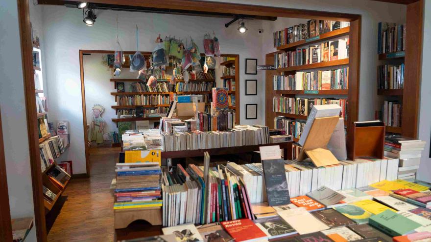 Interior of a bookstore with wooden shelves full of books, display tables, and a children's section in the back decorated with illustrations.