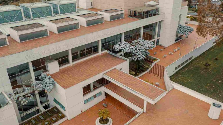 Vista aérea de un moderno centro cultural con terrazas de ladrillo, amplios ventanales y zonas verdes alrededor.