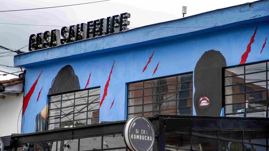 Facade of Casa San Felipe with an urban mural on a blue background depicting human silhouettes and red lines; the name of the place is visible at the top.