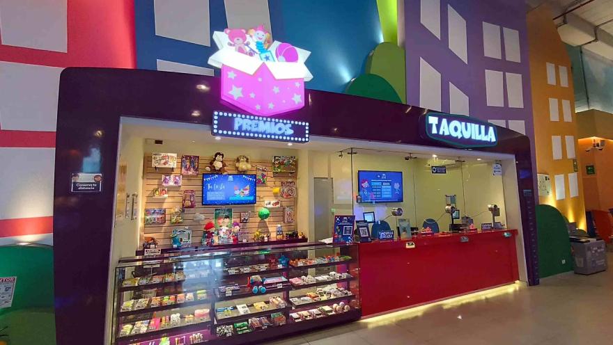  Mostrador de premios y taquilla en un centro de entretenimiento interior, con vitrinas llenas de juguetes y luces coloridas.