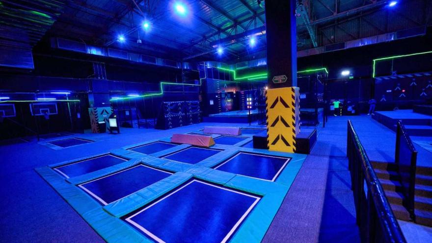 Parque de trampolines en interior con iluminación azul y detalles neón, equipado con varias zonas de salto y obstáculos.