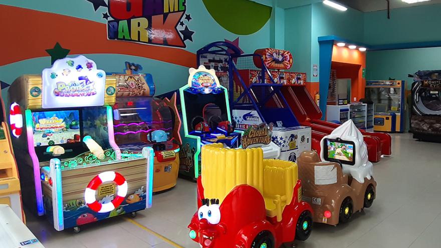  Fila de máquinas arcade en un salón de juegos, con cabinas de conducción, juegos de habilidad y luces neón en un espacio interior.