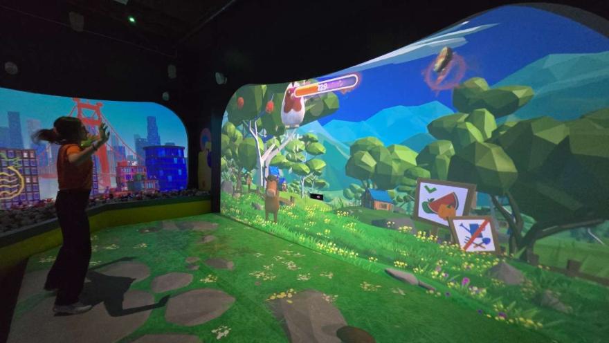 Niños jugando frente a una pantalla interactiva con paisaje desértico animado, rodeados de cubos de colores en un espacio digital inmersivo.